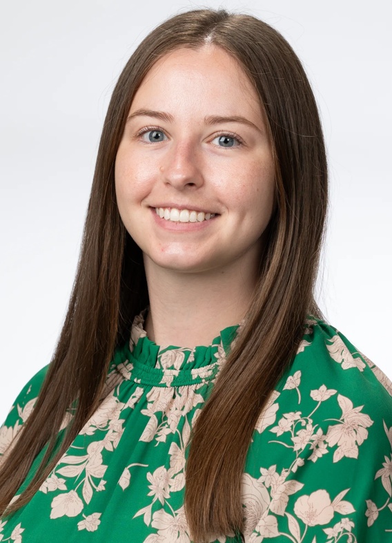 Portrait of Alexa Wawrzyniak, woman with long brown hair and a patterned green shirt.