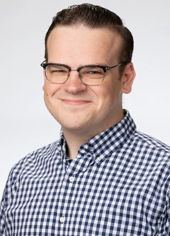 Portrait of Connor Cook, man with short brown hair, glasses, and a striped blue and white shirt.