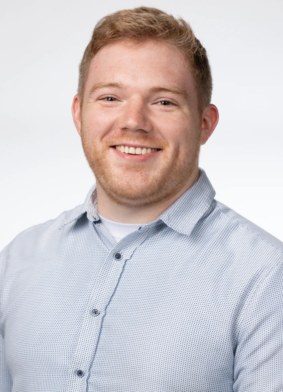 Portrait of Kyle Isaacs, man with short red hair and a grey shirt.