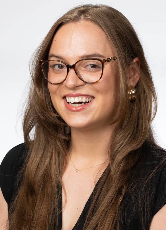 Portrait of McKenzie Alty, woman with long brown hair, glasses, and a black shirt.