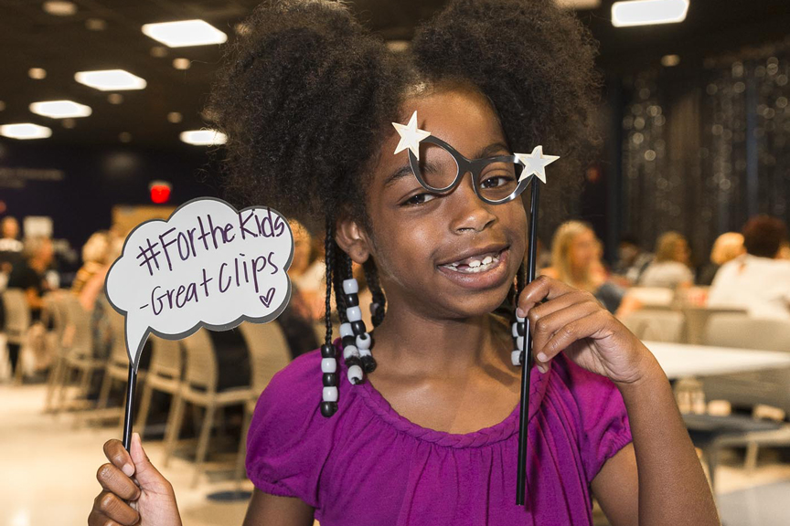 Smiling elementary aged child holding a Great Clips sign