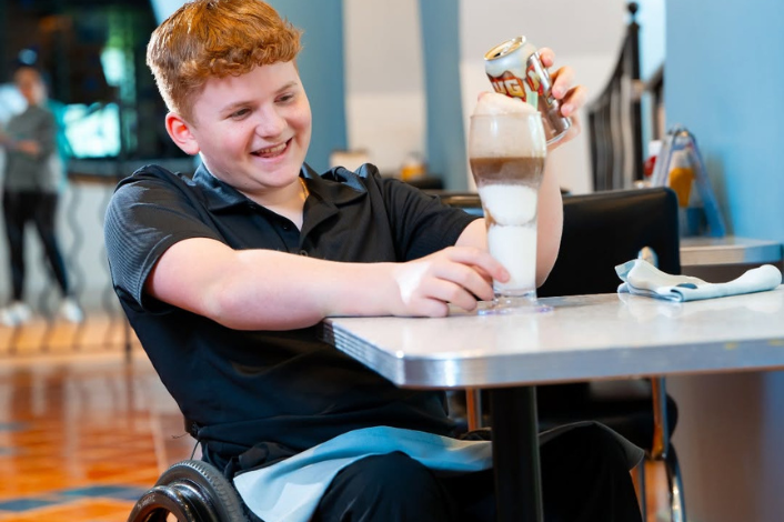 Teen boy pouring root beer into a mug and smiling. 