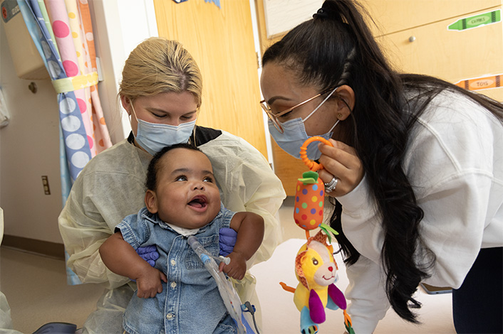 Smiling baby with two nursing staff