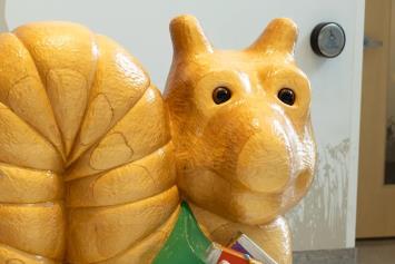 Large, yellow snail sculpture wearing a green shirt, located in a hospital lobby area, serving as a playful seating option for children.