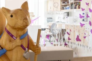 Large sculpture of a squirrel holding a spoon, located in a hospital corridor near patient rooms.