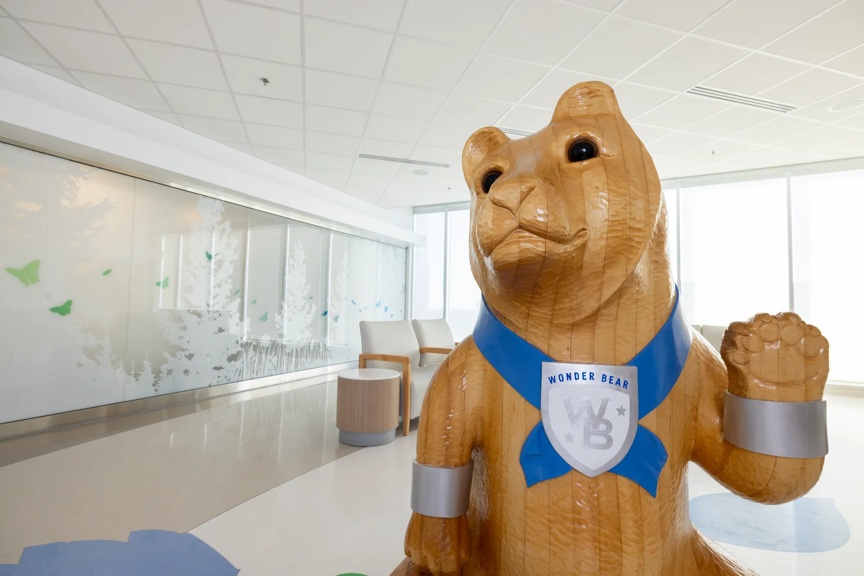 Large wooden bear statue in a hospital waiting area, designed to create a welcoming environment for children.