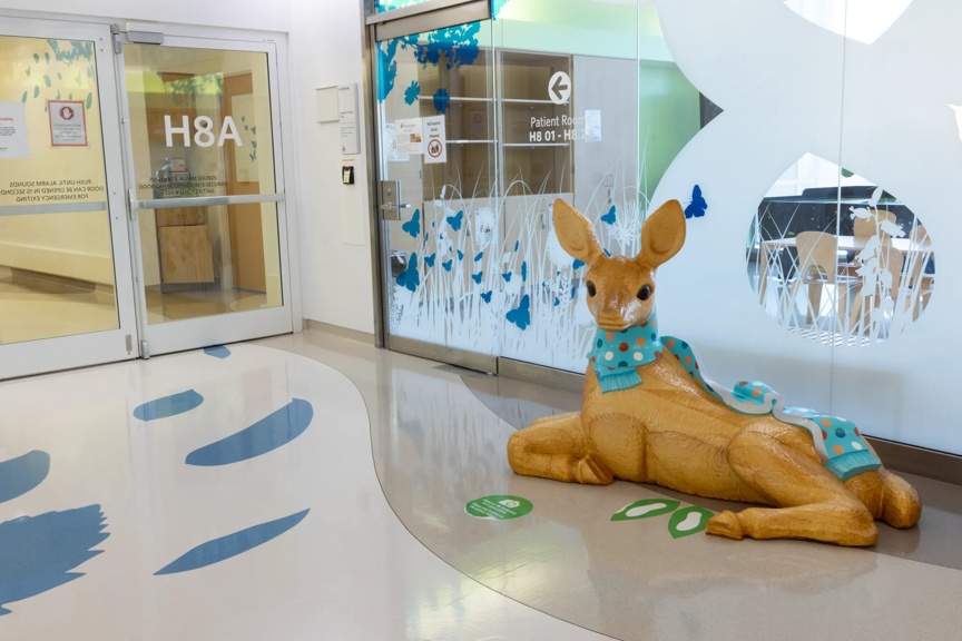 A friendly deer statue wearing a scarf, located near the entrance of a hospital, surrounded by floral designs.