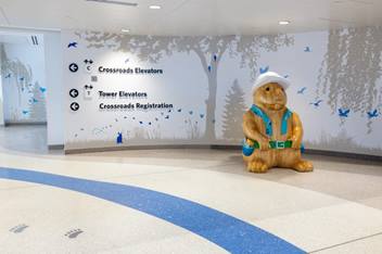 A friendly statue of a large rabbit wearing a hat and vest near directional signs for elevators and registration.