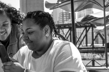 Two teen girls on tablet with city skyline behind them 