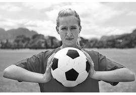 A female soccer player looks determined as she holds a soccer ball in both hands