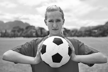 A female soccer player looks determined as she holds a soccer ball in both hands