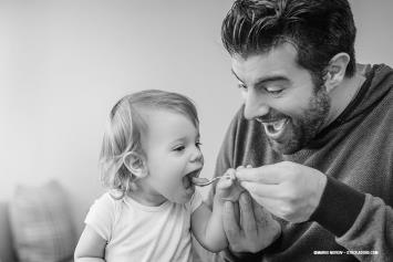A dad helps feed his toddler-aged child with a spoon