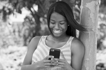 Teenage Girl Leaning on Tree and Looking at Cell Phone