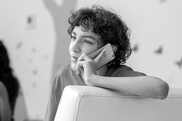Teen Boy Resting In Chair on Phone With Friends in Background