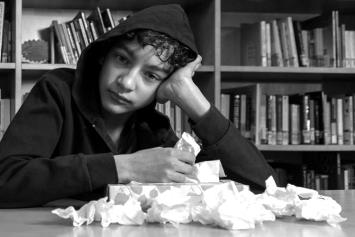 Sick Teen Boy Sitting in Library with Tissues in Hand