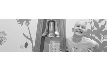 A young girl wearing a t-shirt, smiling by a bell.