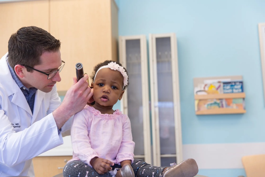 Medical professional using a tool to look into toddler patient's ear. 