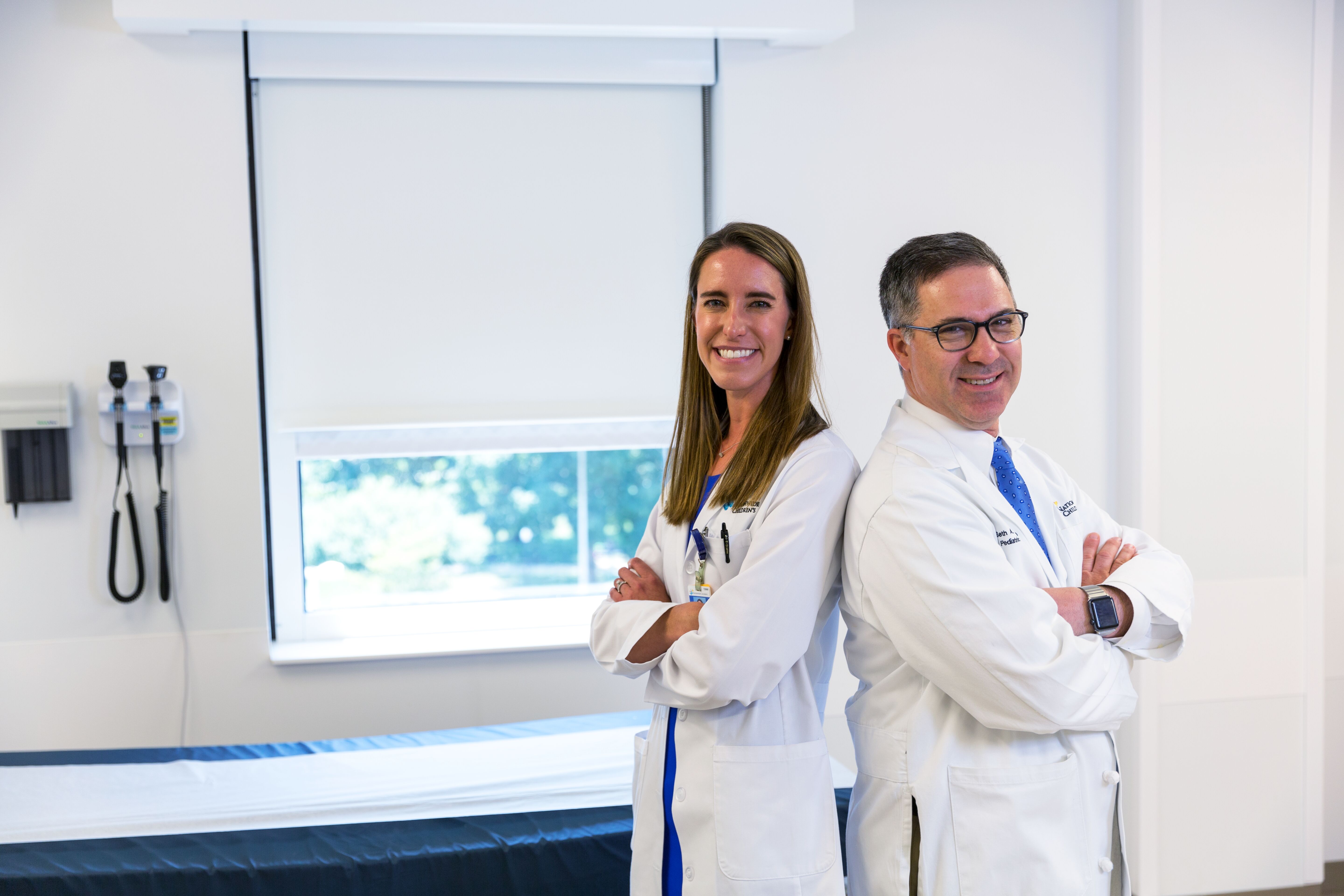 Smiling healthcare professionals pose confidently in a medical examination room, with medical equipment visible in the background.