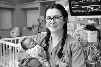 Medical provider with braids in her hair and glasses, holding a baby in the NICU. There are monitors and a crib in the background.