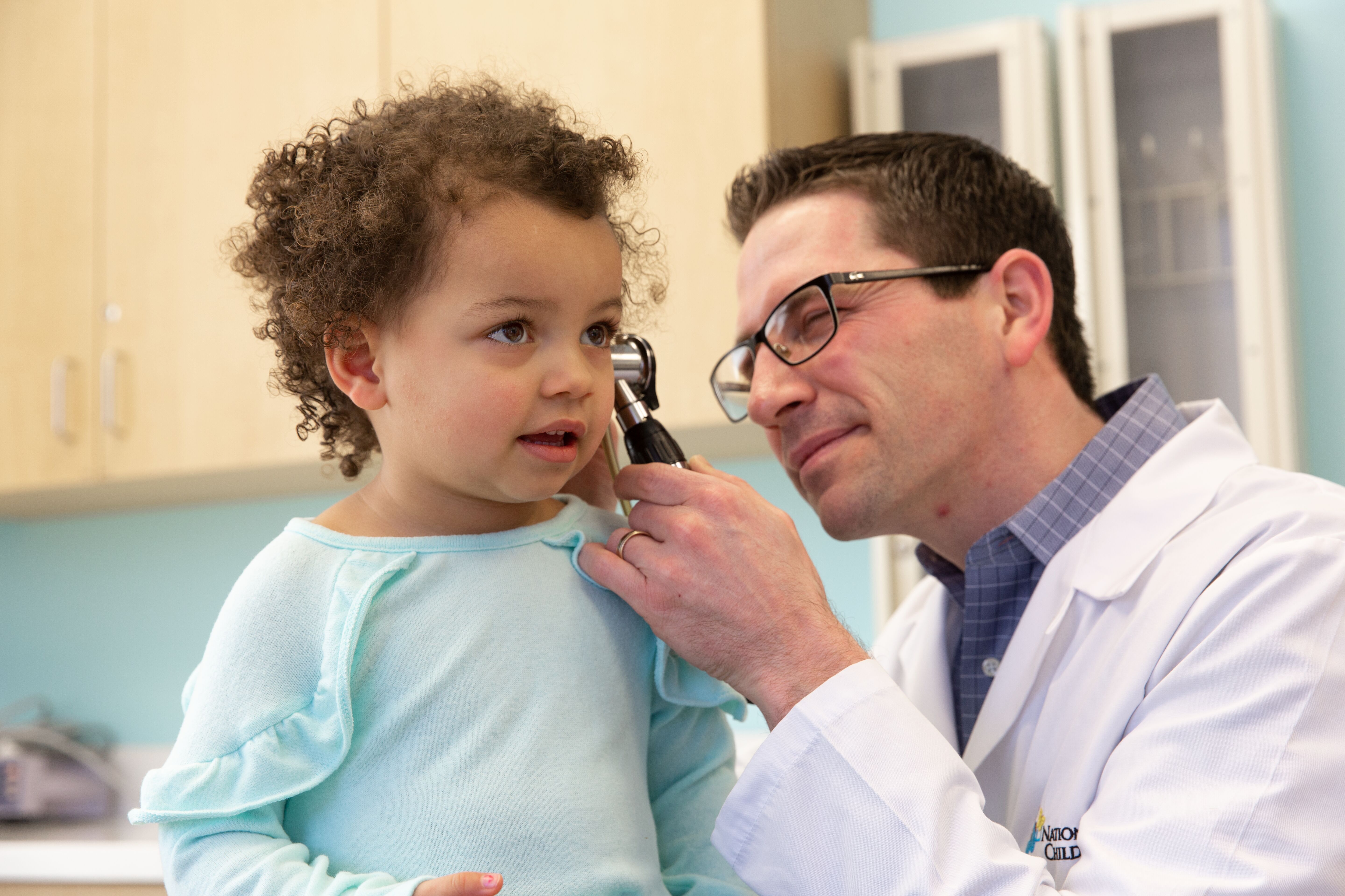 A doctor examines a young child's ear with an otoscope during a check-up in a medical office.