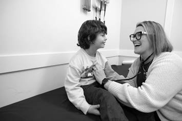 Black and white image of a physician in clinic using a stethoscope on a small child.