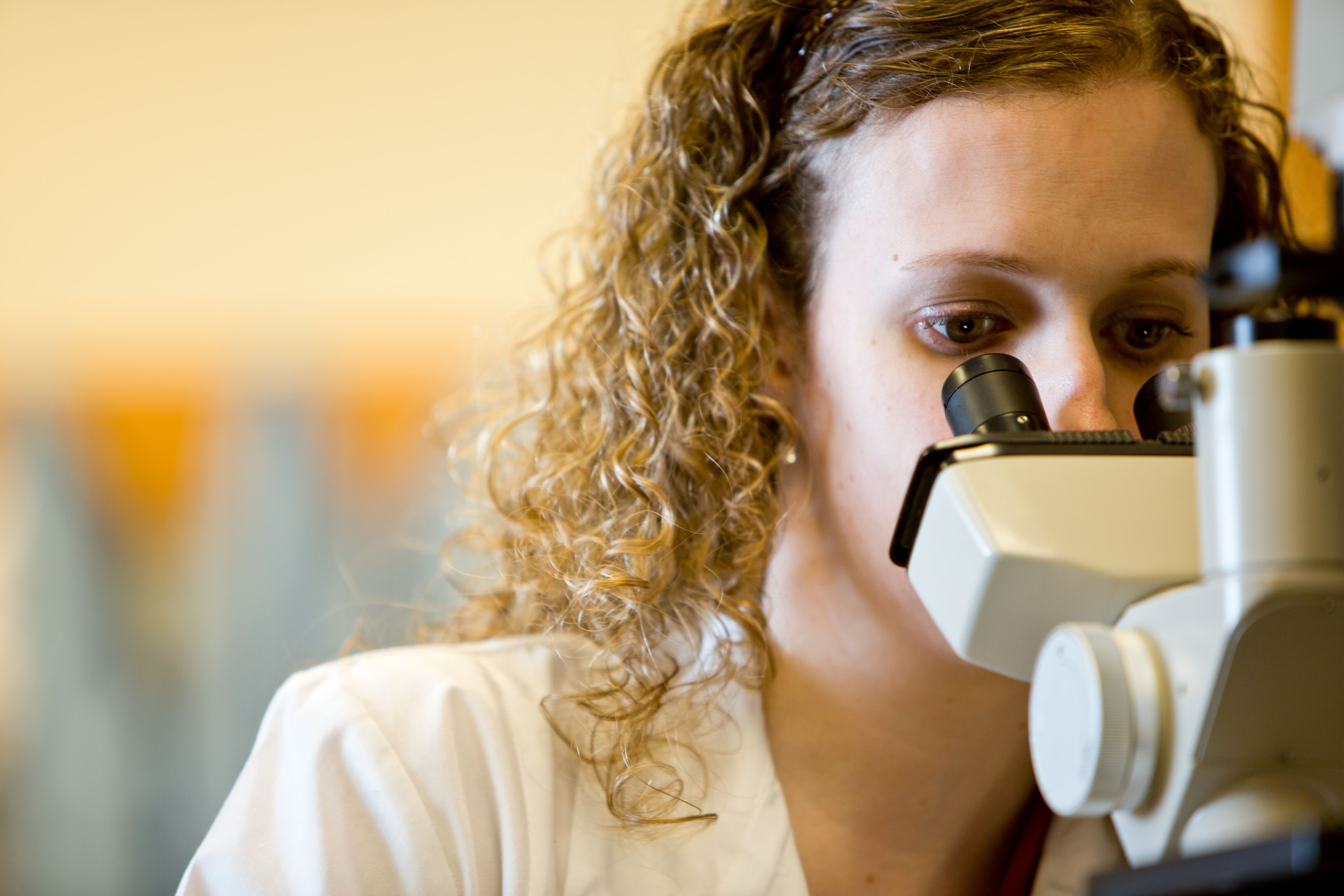 A laboratory technician examines a sample through a microscope, focusing on detailed analysis.