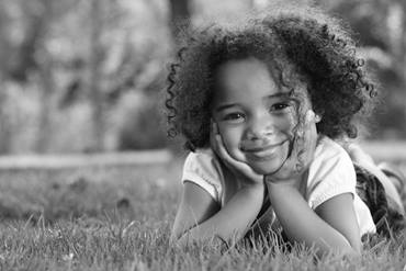 young girl laying in the grass on her stomach with her head resting on her hands