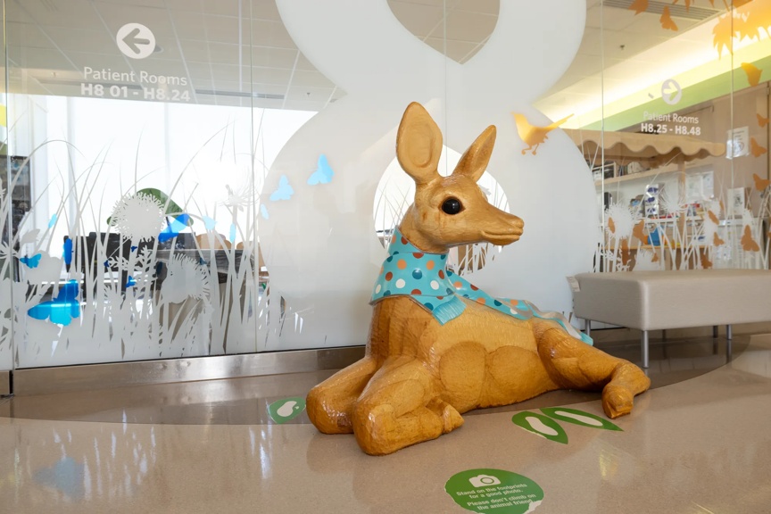 A large, decorative wooden deer wearing a blue polka-dotted scarf sits near the entrance to patient rooms, enhancing the environment.