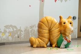 Large, yellow snail sculpture wearing a green shirt, located in a hospital lobby area, serving as a playful seating option for children.
