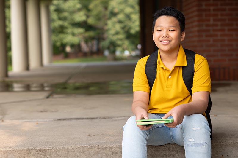 Middle school student with backpack sitting outside a school building