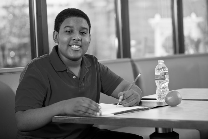 Young Boy Writing At Desk With Snack