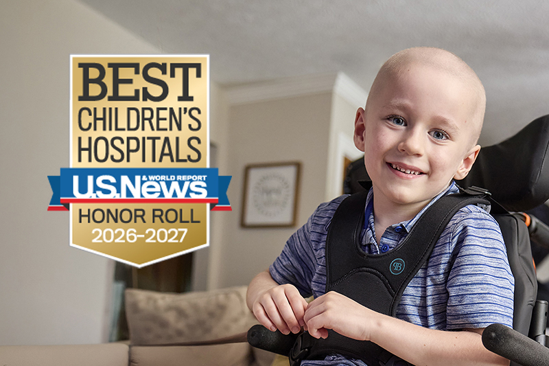 A young boy wearing a striped shirt smiles as he sits in a wheelchair. 
