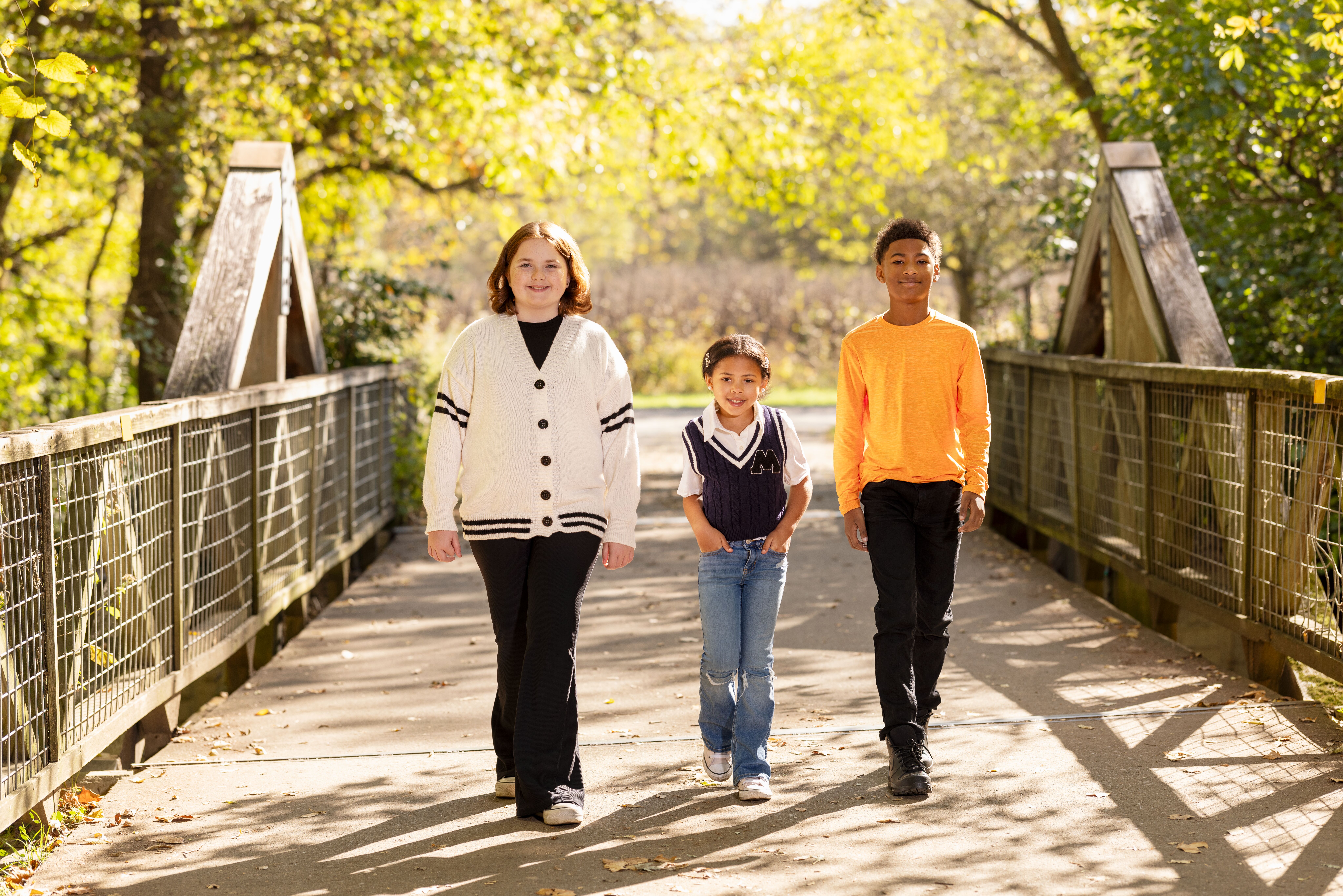 Three preteen children walking across a bridge and smiling.