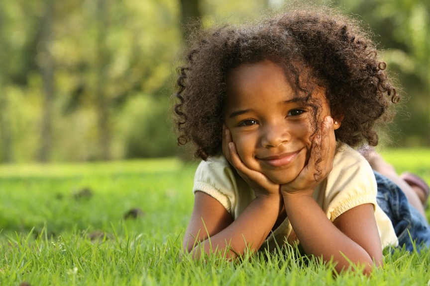 young girl laying in the grass on her stomach with her head resting on her hands