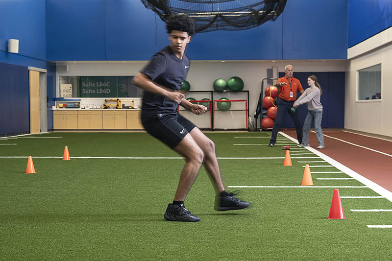 A teenage male athlete completes a drill in an indoor sports medicine facility