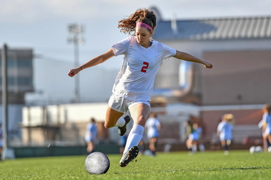 A female teen soccer player in a white kit prepares to kick
