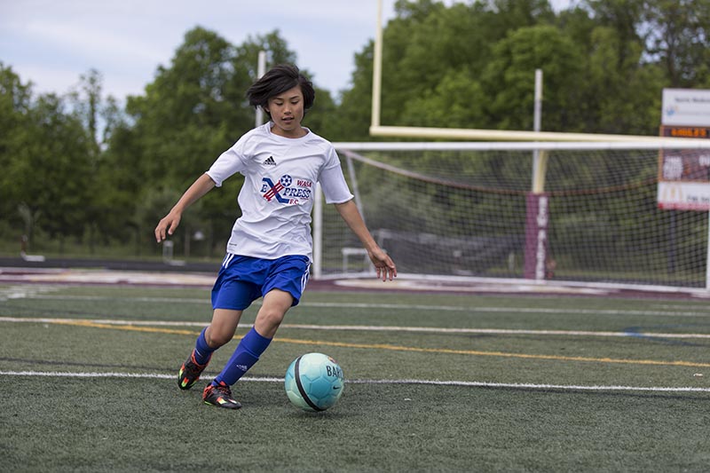 A youth soccer player dribbles a ball on a grassy field during a game or practice session.
