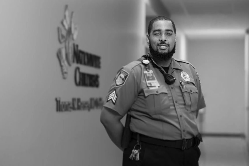 Bashawn is smiling, arms resting behind him. He's wearing a uniform and standing in a long hallway.