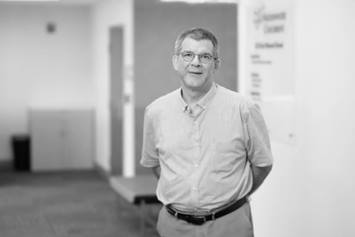 Dr. Rakowsky is standing in a clinic setting. He's smiling and wearing a short-sleeved, button-down collared shirt. He's smiling with arms resting behind his back.
