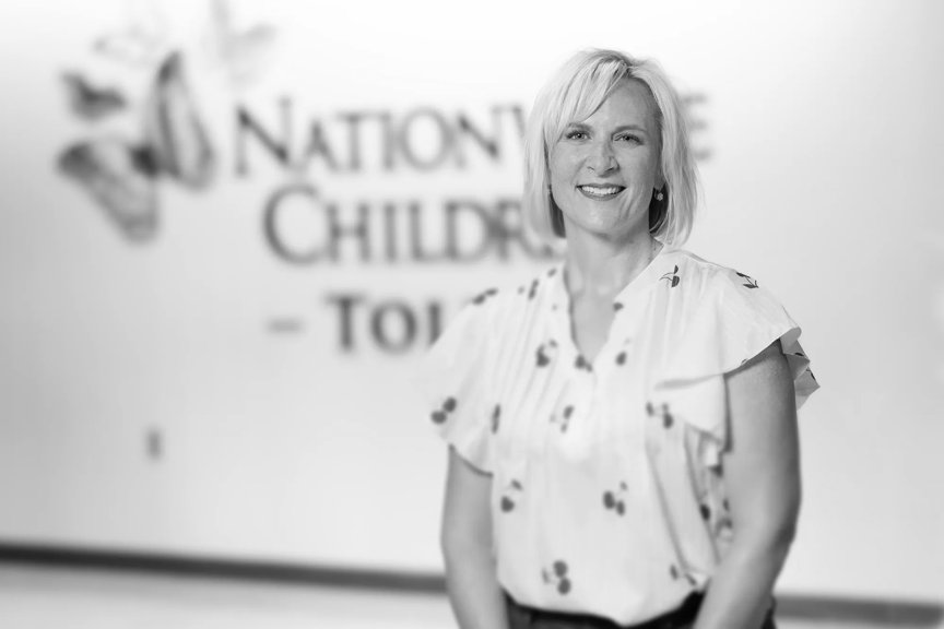 Dr. Stricklen is wearing a light short-sleeve shirt. She's smiling, standing in front of a wall with the Nationwide Children's Toledo logo on it.