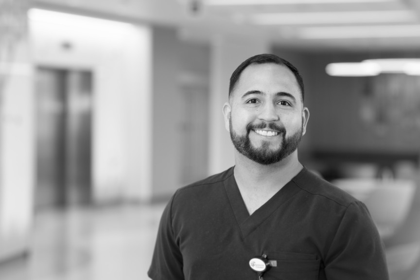 Eduardo is smiling, wearing scrubs, standing in a clinic setting.