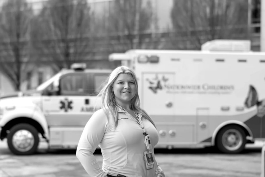 Lily is smiling, standing outside in front of a Nationwide Children's ambulance.