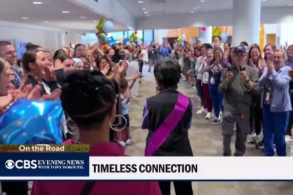 Wynola wears a purple sash and walks through a large crowd that's cheering and celebrating her.