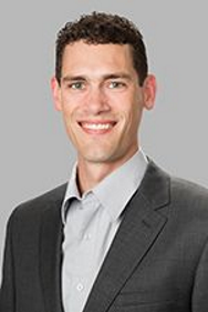 Portrait of Johnathan Carlson. Johnathan is wearing a light gray button up shirt with a dark gray jacket. 