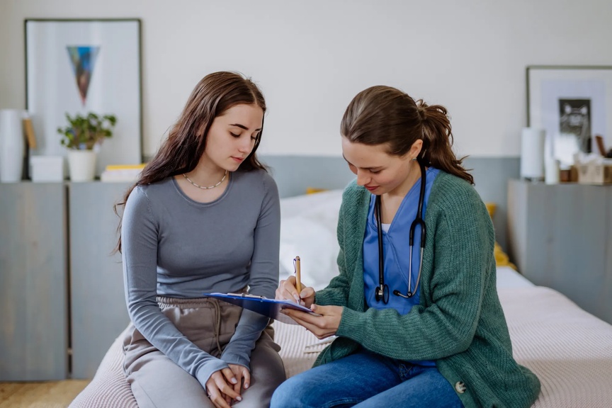 Teenage girl having stomach ache, young doctor examining her.