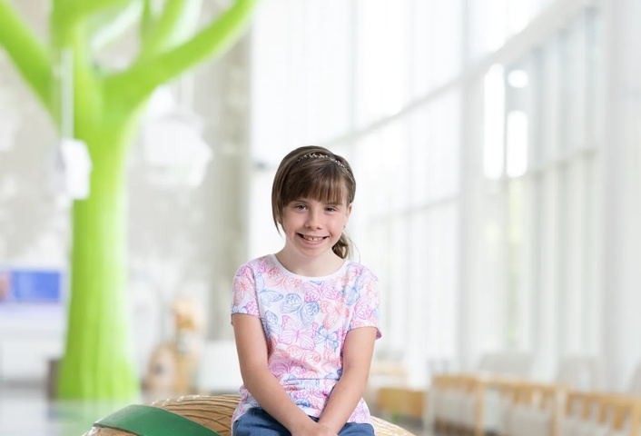 A child sits on a turtle-shaped seating area in a hospital atrium, promoting a friendly environment for young visitors.