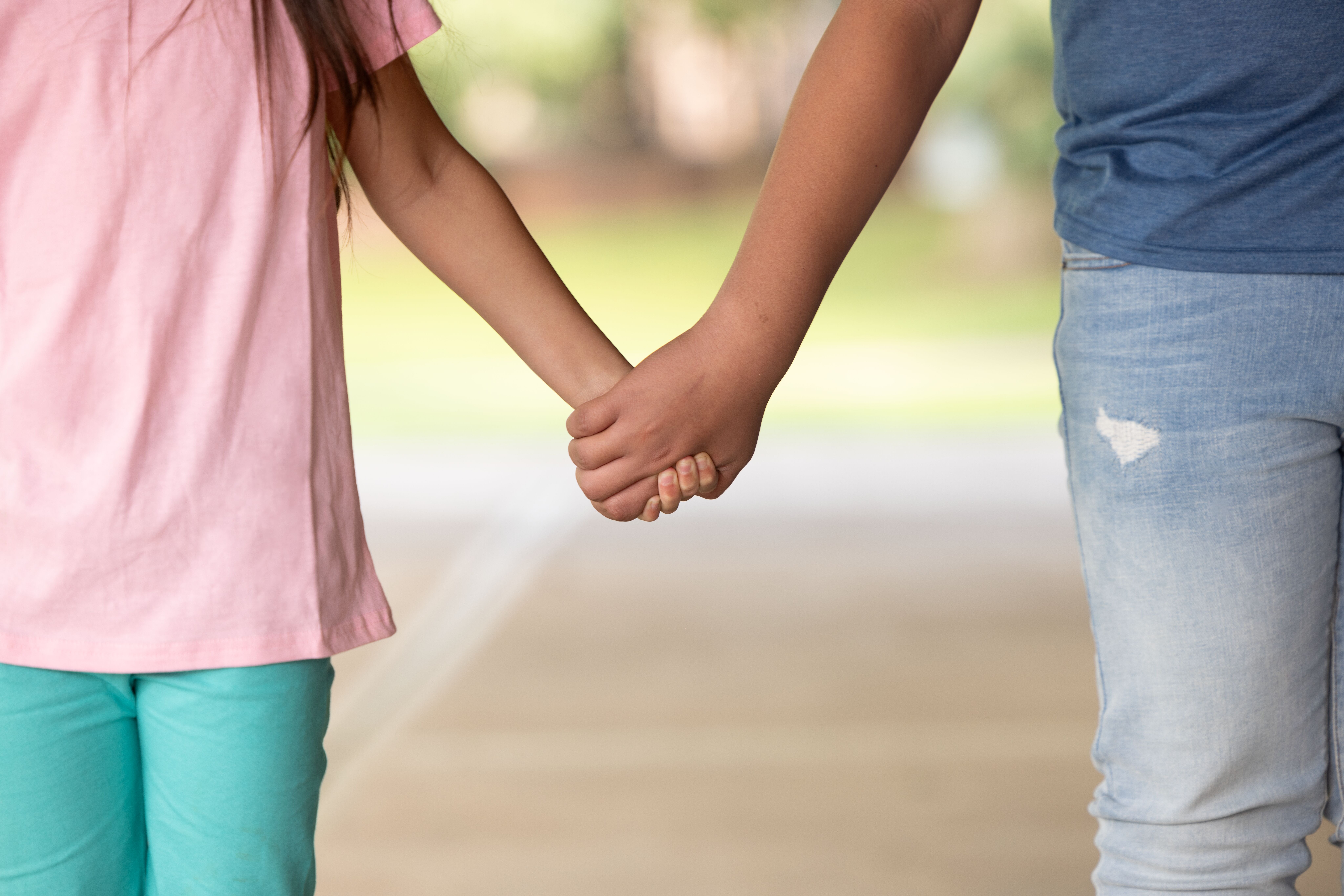Two children holding hands while walking together outdoors, symbolizing support and connectio