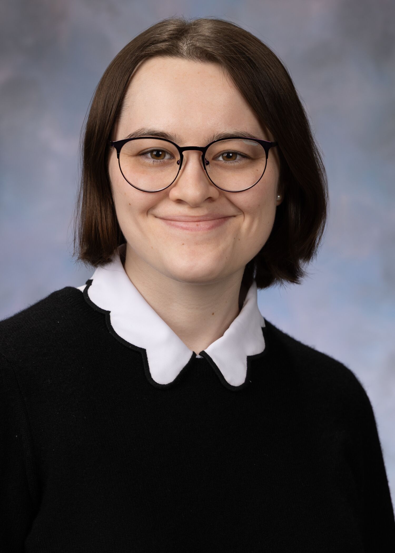 Portrait of Shannon Henderson. Shannon has short brown hair and is wearing a black shirt with a white collar. 