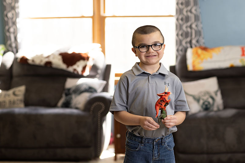 A young boy wearing glasses smiles as he plays with toy dinosaurs.