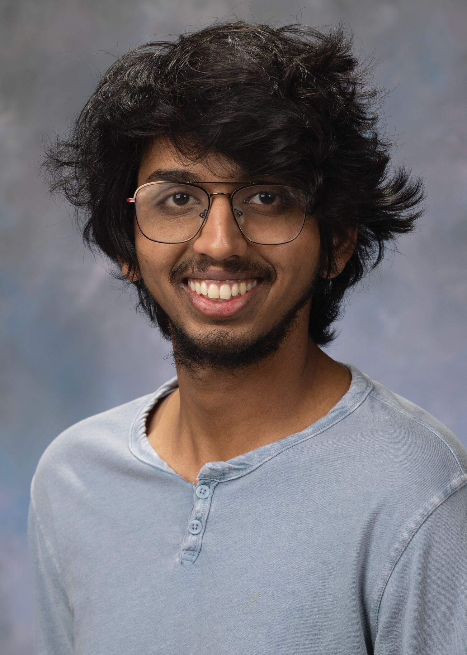 Portrait of Apoorv Vinod Thakre. Apoorv is wearing glasses and a blue gray shirt.